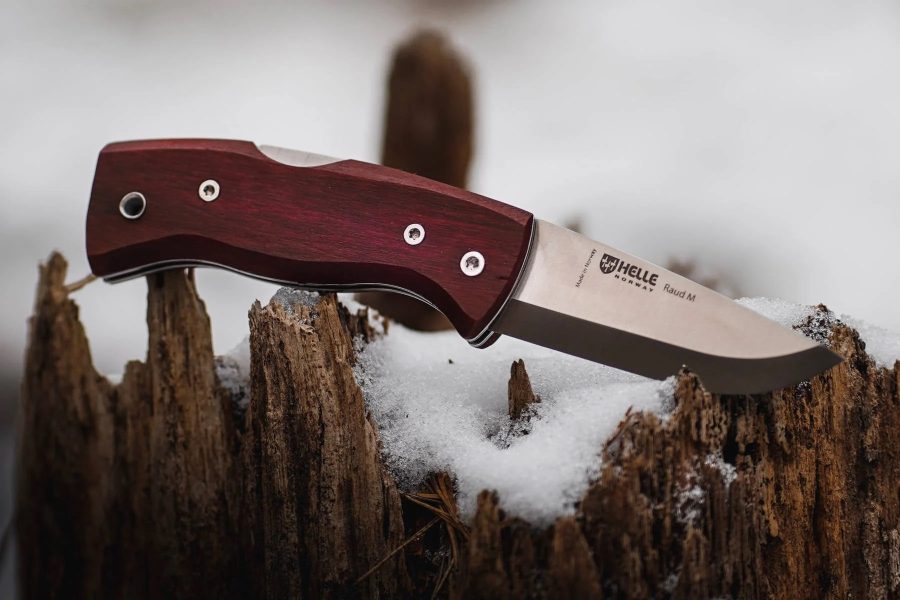 Wood-handled folding knife in open position, resting on a snow-covered stump.